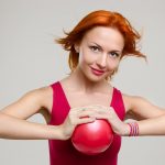 Девушка сжимает мяч ладонями, напрягая мышцы груди