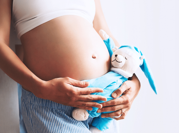 Беременная женщина с мягкой игрушкой в руках возле живота