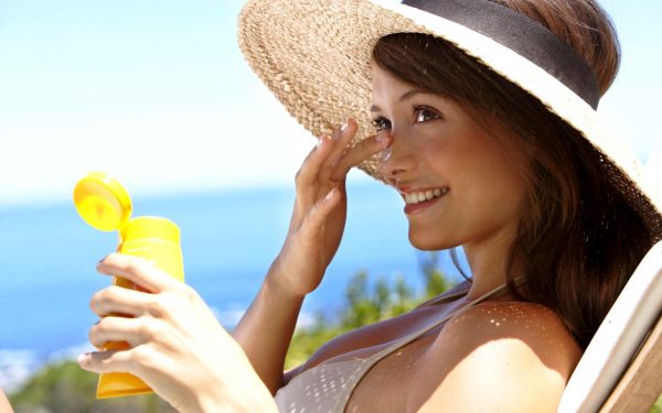 Женщина мажет лицо солнцезащитным кремом
